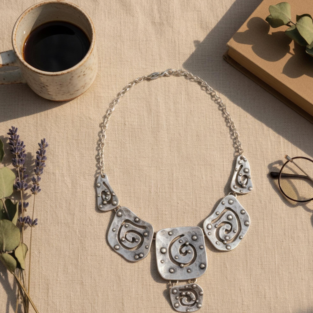 Artisan crafted silver bib necklace featuring hammered texture and geometric swirls.