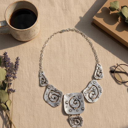 Artisan crafted silver bib necklace featuring hammered texture and geometric swirls.