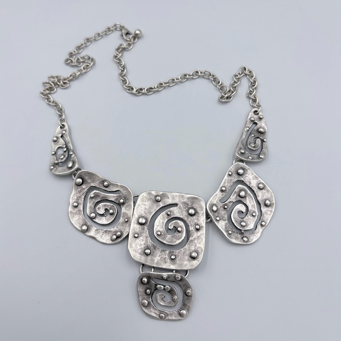 Modern silver jewelry featuring five connected hammered metal plates with swirls.
