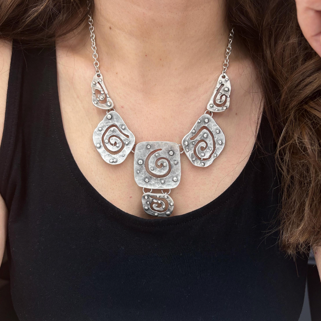 Close-up of a handmade silver statement necklace with intricate spiral cut-outs.