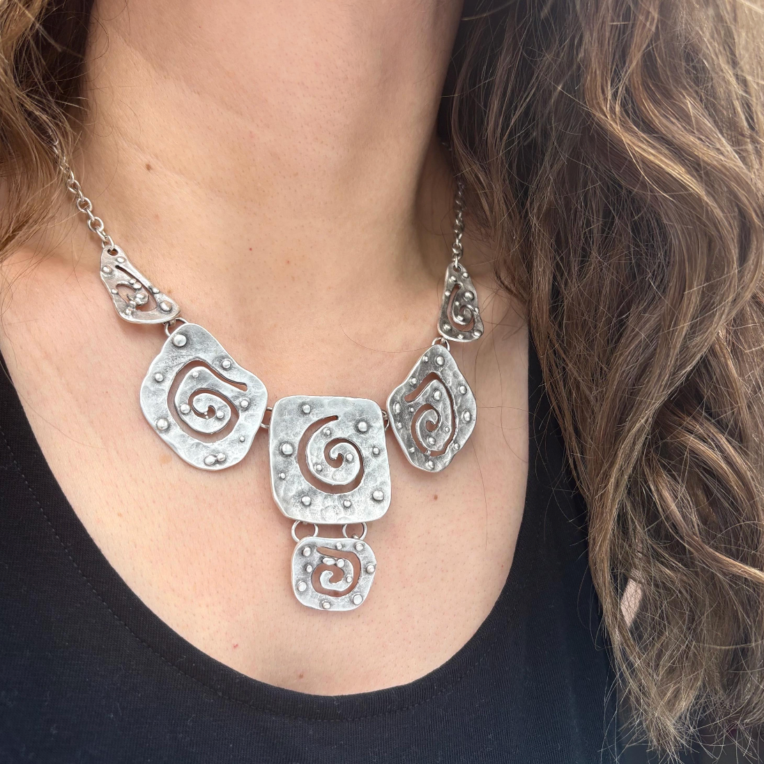 Modern silver jewelry featuring five connected hammered metal plates with swirls.
