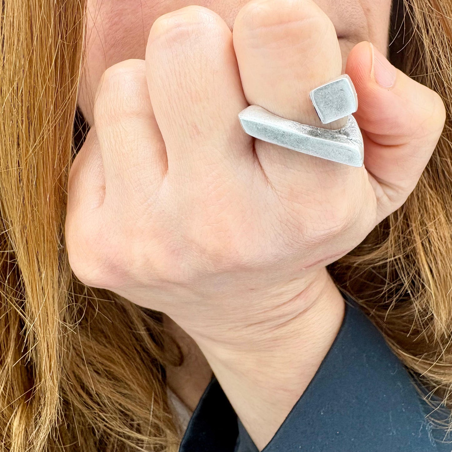 Close-up of a hand wearing a clear stone ring with long hair in the background