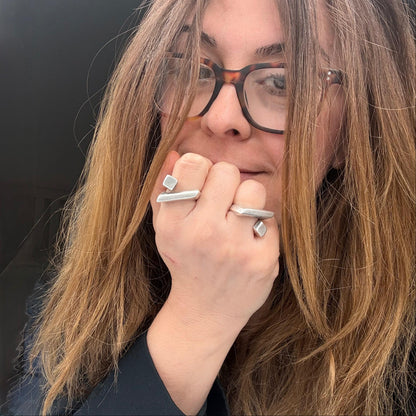 Person with long hair wearing glasses and multiple rings on a black background