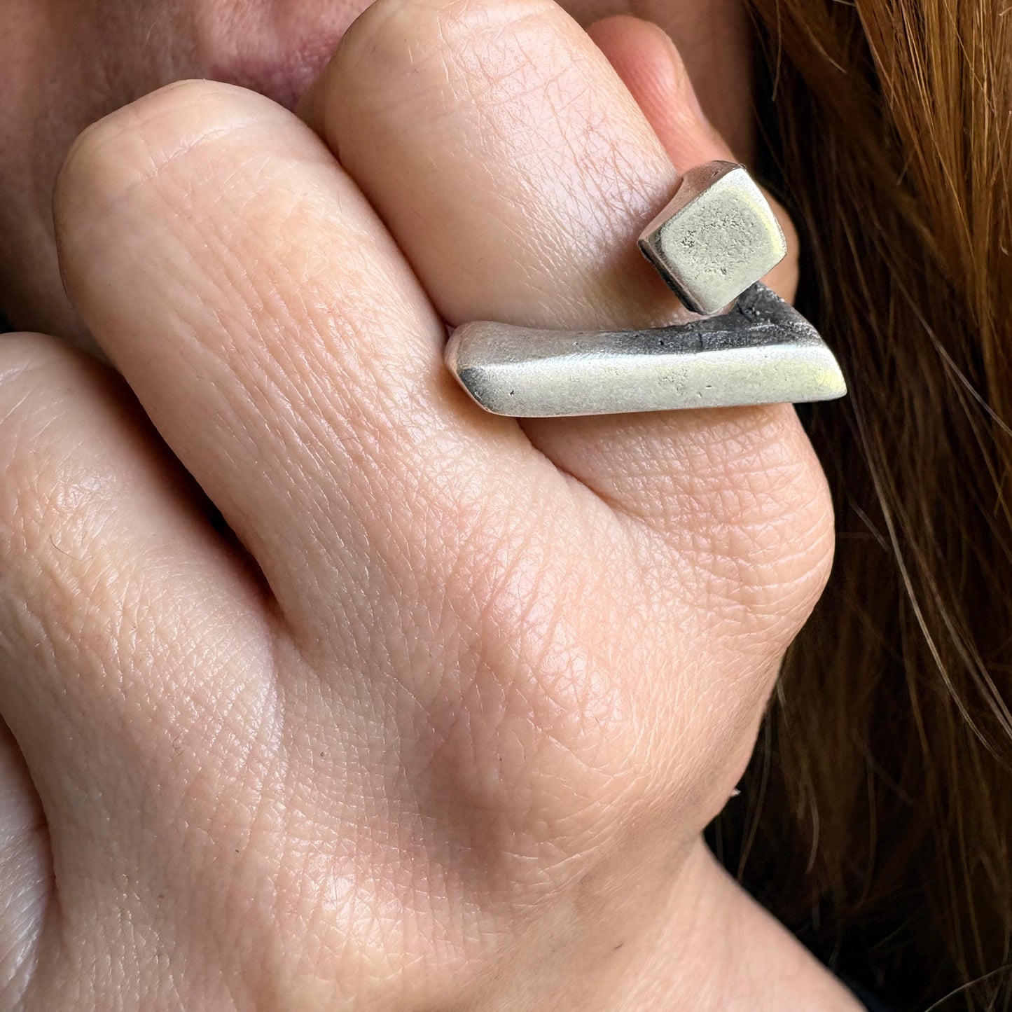 Close-up of a hand wearing a silver ring with a stone on a blurred background