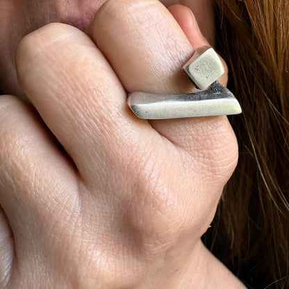 Close-up of a hand wearing a silver ring with a stone on a blurred background