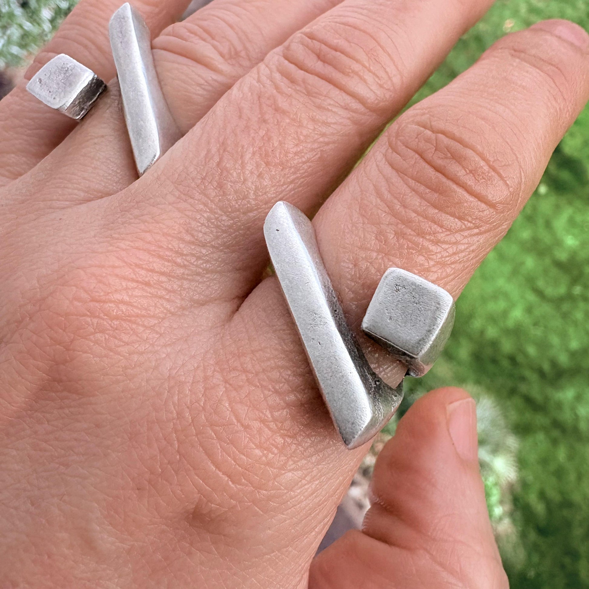 Hand wearing three silver rings with a blurred green background